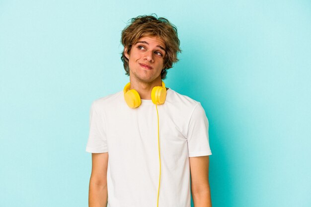 Young caucasian man listening to music isolated on blue background  dreaming of achieving goals and purposes