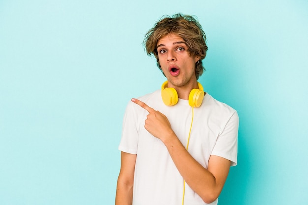 Young caucasian man listening to music isolated on blue background  pointing to the side