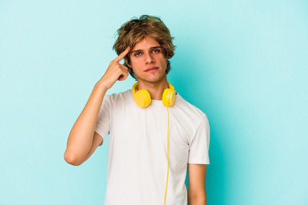 Young caucasian man listening to music isolated on blue background  pointing temple with finger, thinking, focused on a task.