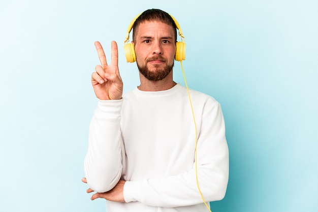 Young caucasian man listening to music isolated on blue background showing number two with fingers.