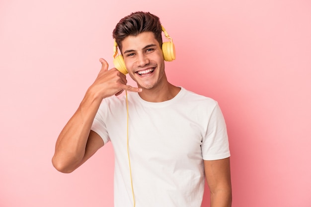 指で携帯電話の呼び出しジェスチャーを示すピンクの背景に分離された音楽を聞いている若い白人男性。