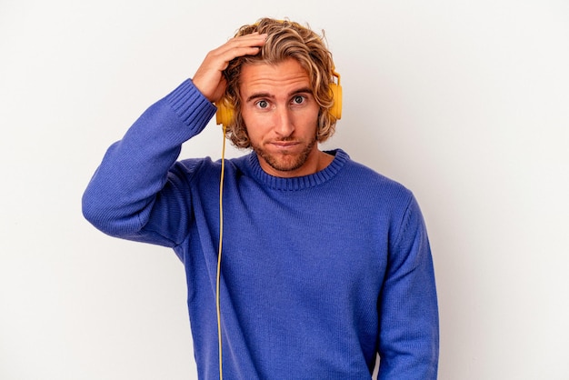 Young caucasian man listening to music isolated on white background being shocked, she has remembered important meeting.