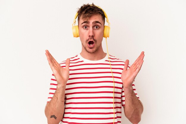 Young caucasian man listening to music isolated on white background surprised and shocked.