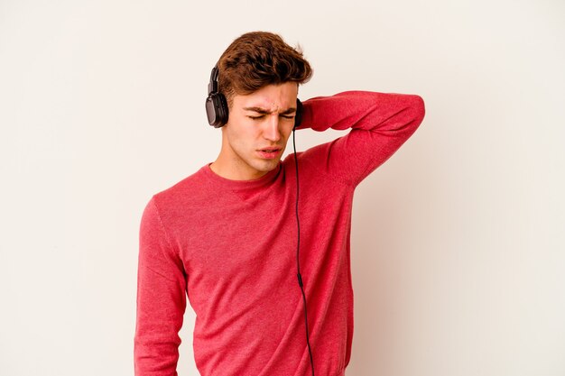 Young caucasian man listening to music isolated on white wall suffering neck pain due to sedentary lifestyle