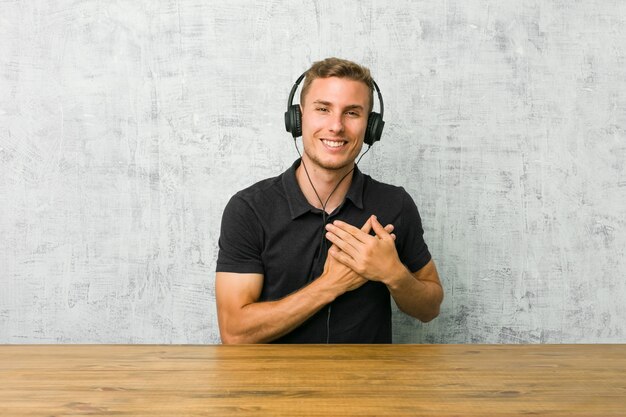 Young caucasian man listening to music with headphones has friendly expression, pressing palm to chest. Love concept.