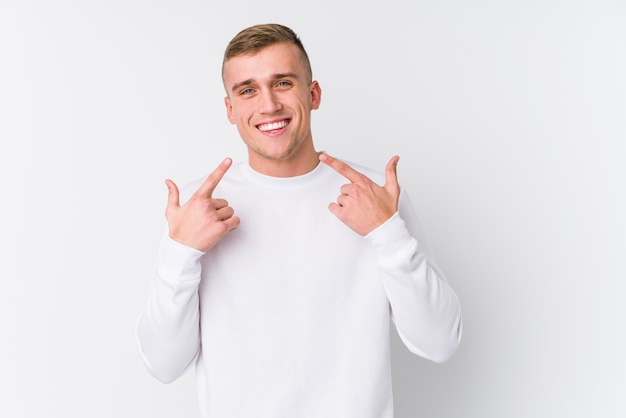 Фото Молодой человек кавказской на белом фоне улыбается, указывая пальцами на рот.