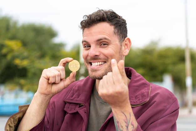 Young caucasian man at outdoors holding a Bitcoin