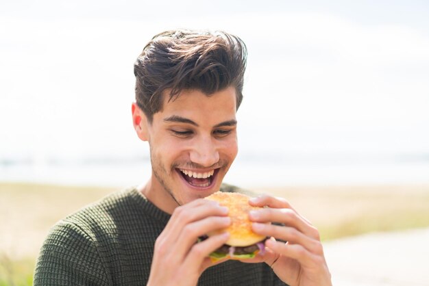 Young caucasian man at outdoors holding a burger