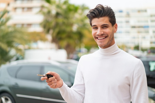 幸せそうな表情で車のキーを保持している屋外で若い白人男性