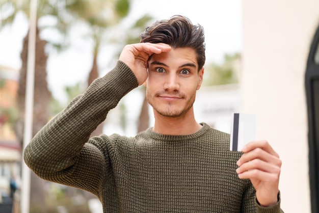 Young caucasian man at outdoors holding a credit card and with sad expression