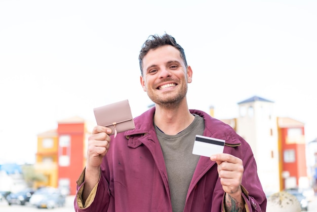 Молодой кавказский мужчина на улице с кошельком и кредитной картой