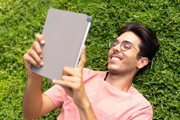 Young caucasian man at outdoors in a park holding a tablet with happy expression