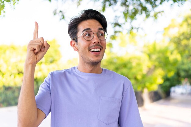 Young caucasian man at outdoors in a park intending to realizes the solution while lifting a finger up