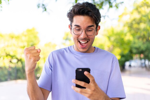 Photo young caucasian man at outdoors in a park surprised and sending a message