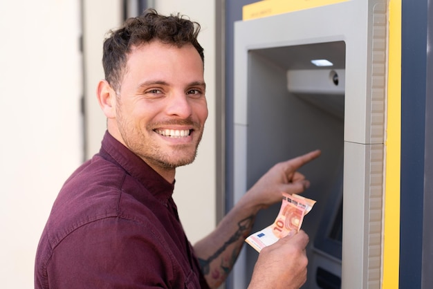 Photo young caucasian man at outdoors using an atm