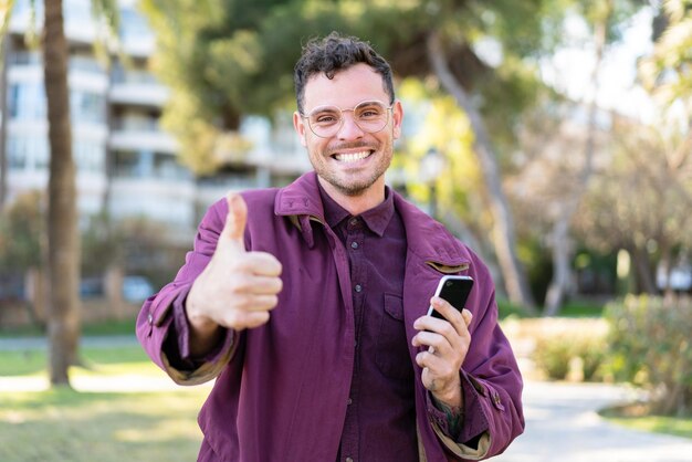 Young caucasian man at outdoors using mobile phone while doing thumbs up