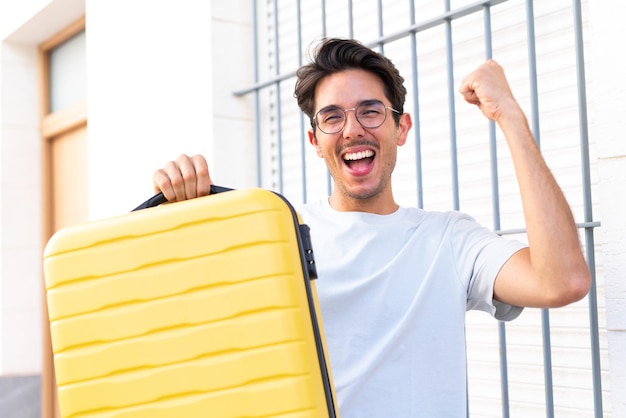 Young caucasian man at outdoors in vacation with travel suitcase