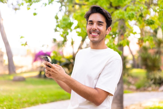 Giovane uomo caucasico in un parco che invia un messaggio o un'e-mail con il cellulare