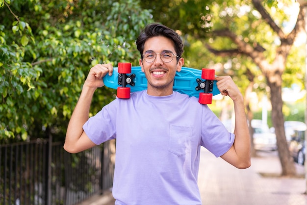 Young caucasian man in a park with a skate with happy expression