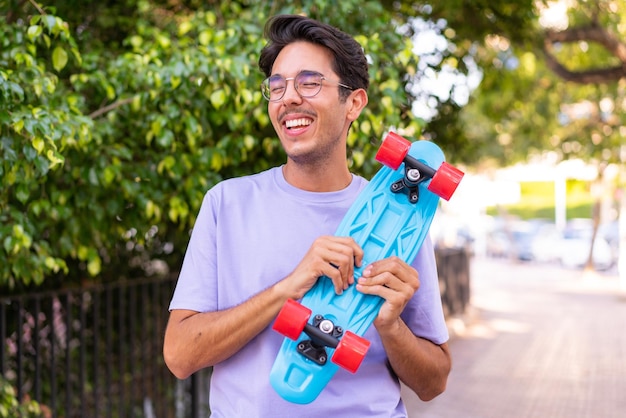 Young caucasian man in a park with a skate with happy expression