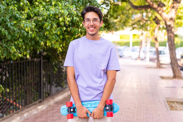 Young caucasian man in a park with a skate with happy expression