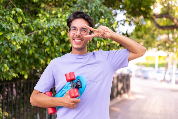 Young caucasian man in a park with a skate with happy expression