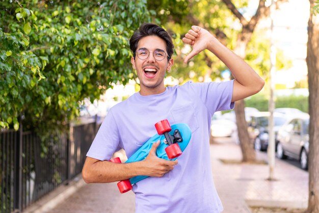 Young caucasian man in a park with a skate with happy expression