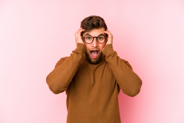 Young caucasian man on pink wall screaming, very excited, passionate, satisfied with something.