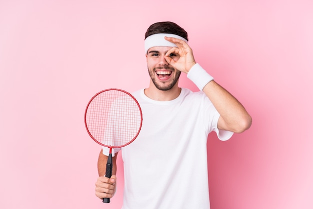 Il giovane uomo caucasico che gioca a badminton ha isolato eccitato mantenendo il gesto giusto sull'occhio.