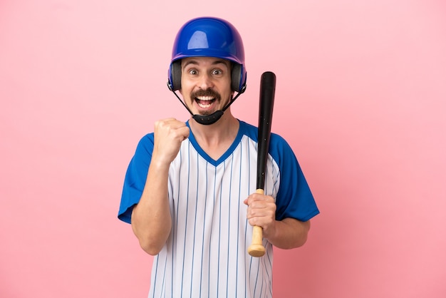 Young caucasian man playing baseball isolated on pink background celebrating a victory in winner position