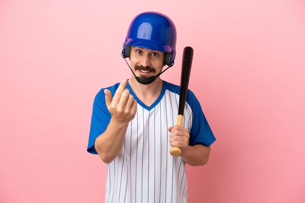 Young caucasian man playing baseball isolated on pink background doing coming gesture