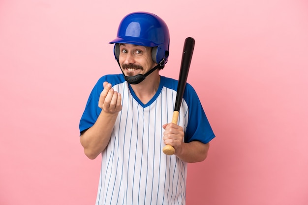 Young caucasian man playing baseball isolated on pink background making money gesture