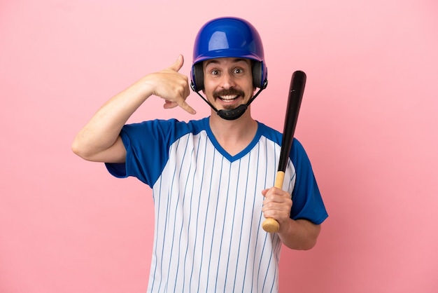 Young caucasian man playing baseball isolated on pink background making phone gesture. Call me back sign