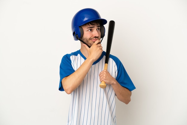 Young caucasian man playing baseball isolated on white background having doubts and thinking