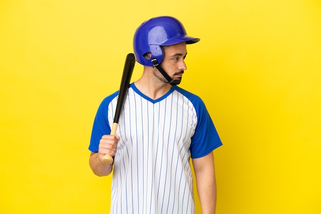 Foto giovane uomo caucasico che gioca a baseball isolato su sfondo giallo guardando di lato