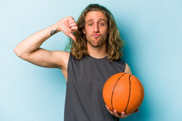 Young caucasian man playing basketball isolated on blue background showing a dislike gesture thumbs down Disagreement concept