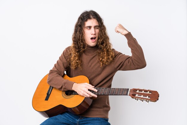 Young caucasian man playing guitar isolated raising fist after a victory, winner concept.