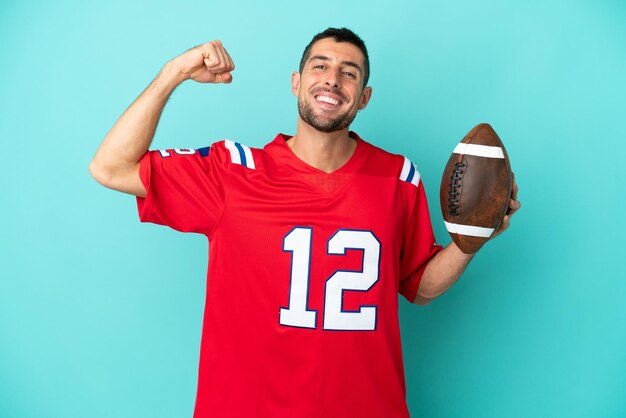 Young caucasian man playing rugby isolated on blue background doing strong gesture