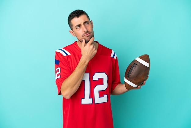 Young caucasian man playing rugby isolated on blue background having doubts