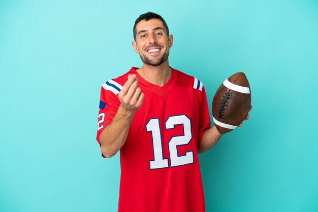 Young caucasian man playing rugby isolated on blue background\
making money gesture