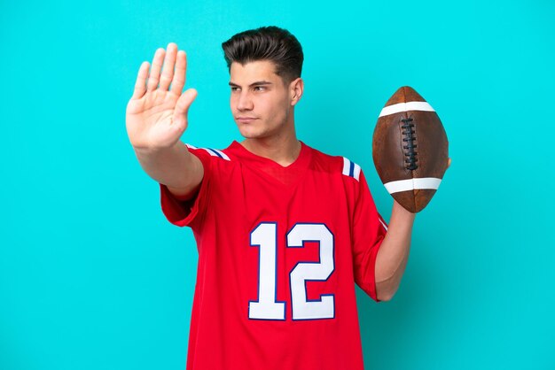 Young Caucasian man Playing rugby isolated on blue background making stop gesture and disappointed