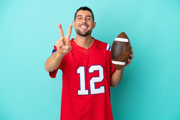 Young caucasian man playing rugby isolated on blue background smiling and showing victory sign