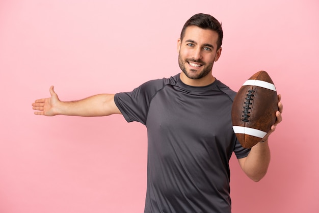 Young caucasian man playing rugby isolated on pink background extending hands to the side for inviting to come