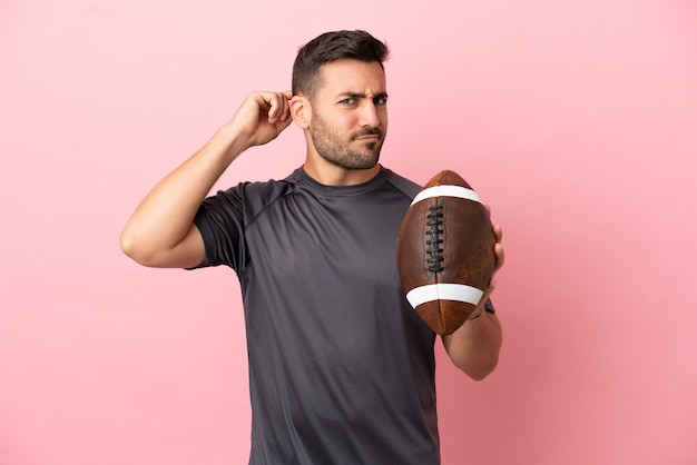 Young caucasian man playing rugby isolated on pink background having doubts