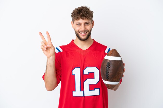 Young caucasian man playing rugby isolated on white background smiling and showing victory sign