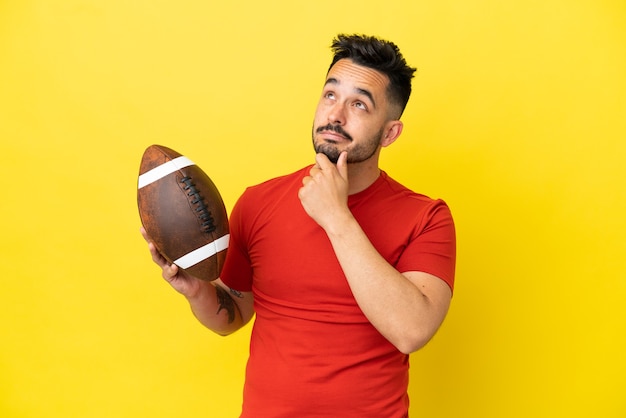 Young Caucasian man playing rugby isolated on yellow background having doubts
