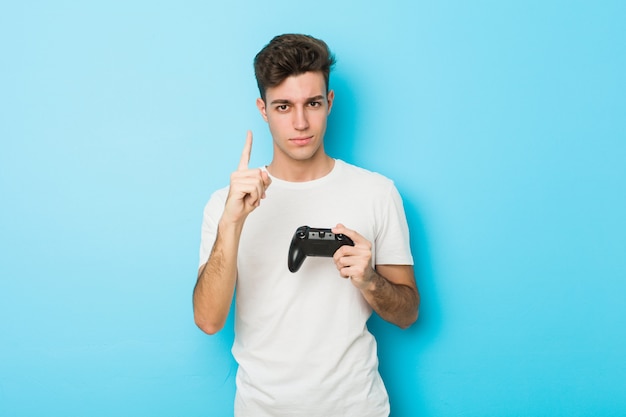 Young caucasian man playing videogames with game controller showing number one with finger.