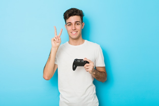Молодой кавказский человек играя видеоигры с регулятором игры показывая номер два с пальцами.