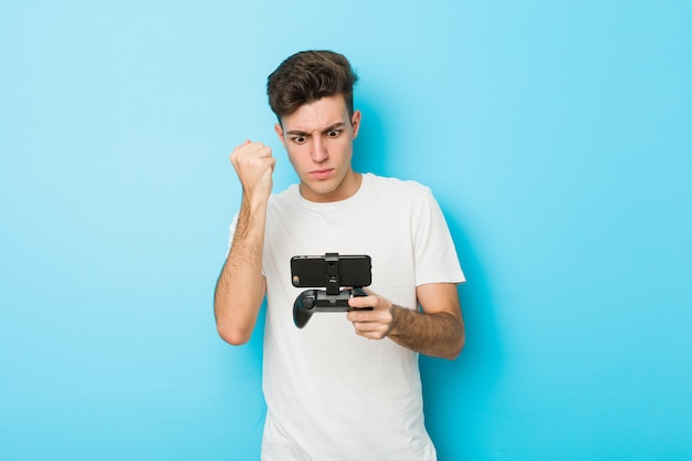 Young caucasian man playing videogames with phone showing fist to camera, aggressive facial expression.