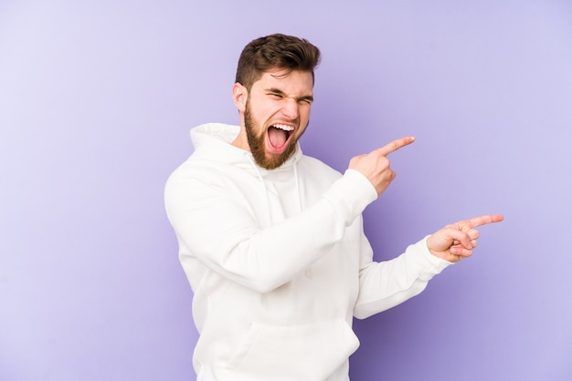 Young caucasian man pointing with forefingers to a copy space, expressing excitement and desire.